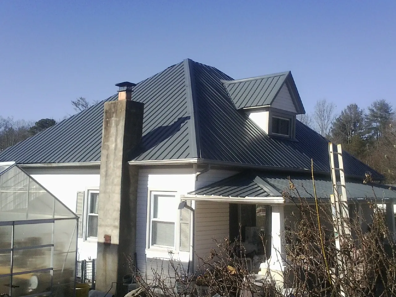 Dark blue standing seam metal roof on a white farmhouse with dormer — Slate & Tile Roof Repair by Roofing Brothers in Aldrich