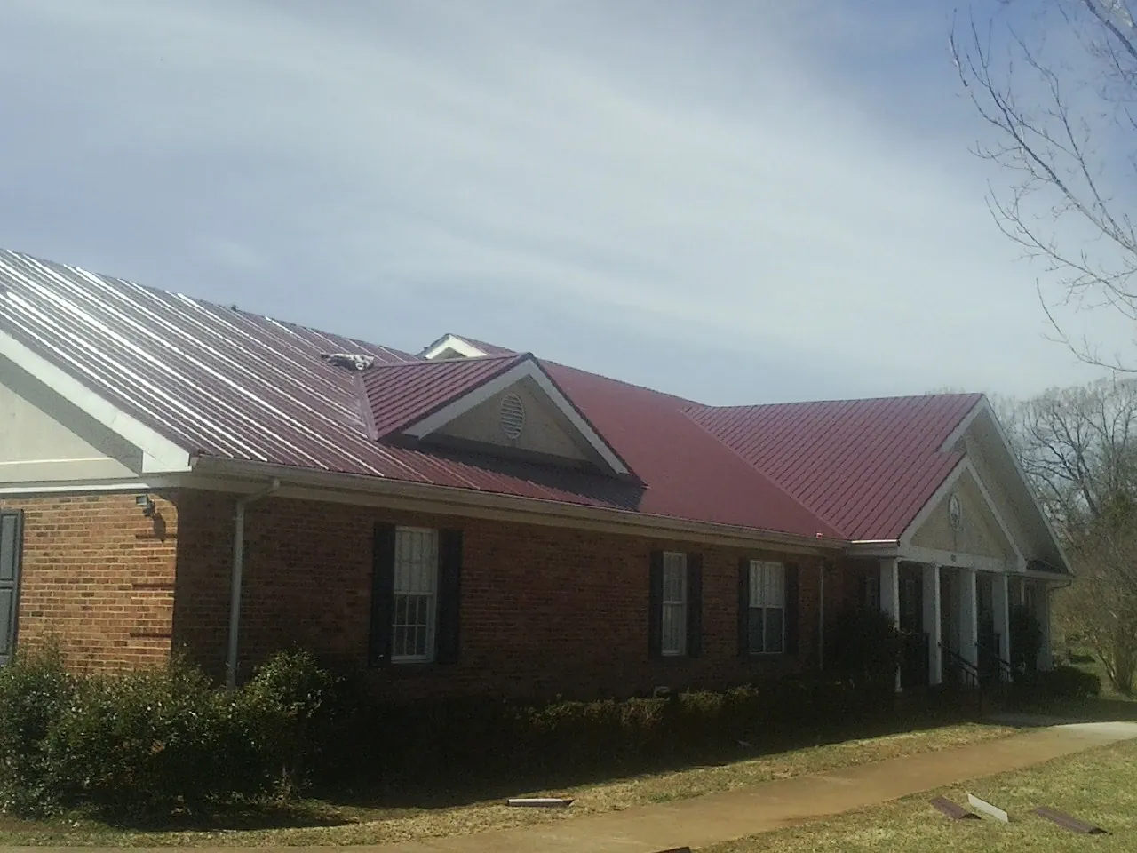 Red metal roof with gabled entries on a long brick building, from a Hail Damage Roof Repair job in Aldrich