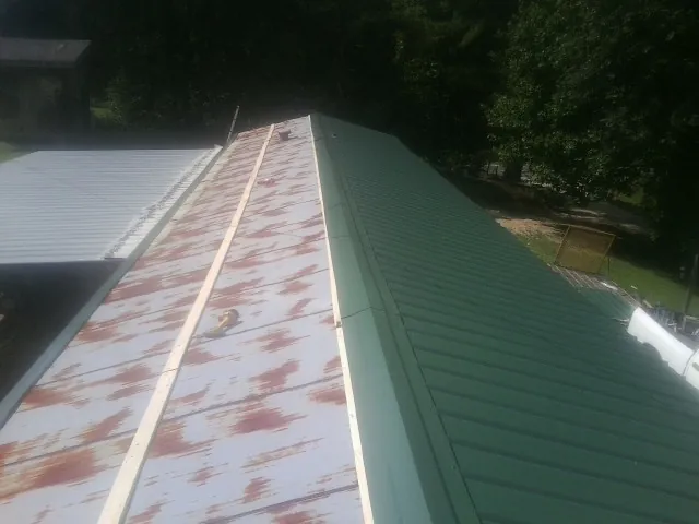 Old rusted panels beside newly installed green metal roofing — Wind Damage Roof Repair by Roofing Brothers in Aldrich