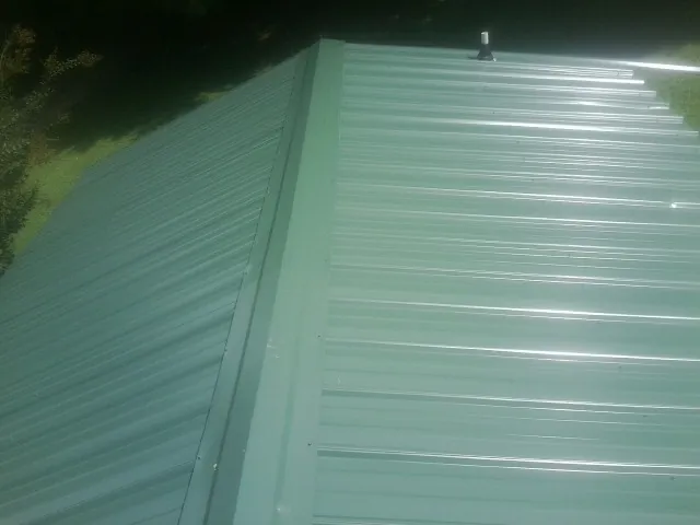 New green metal panels meeting at the ridge of a roof — Flat Roof Repair work by our crew in Aldrich