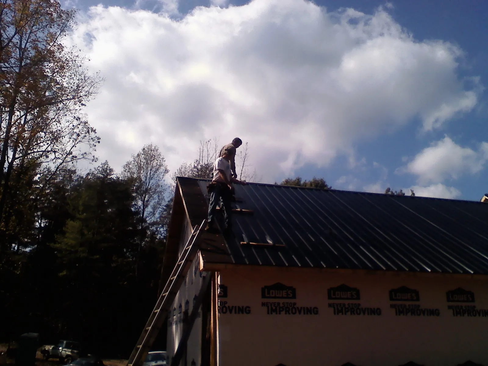Roofer fastening dark metal panels high against a cloudy sky, from a Roof Inspection job in Aldrich