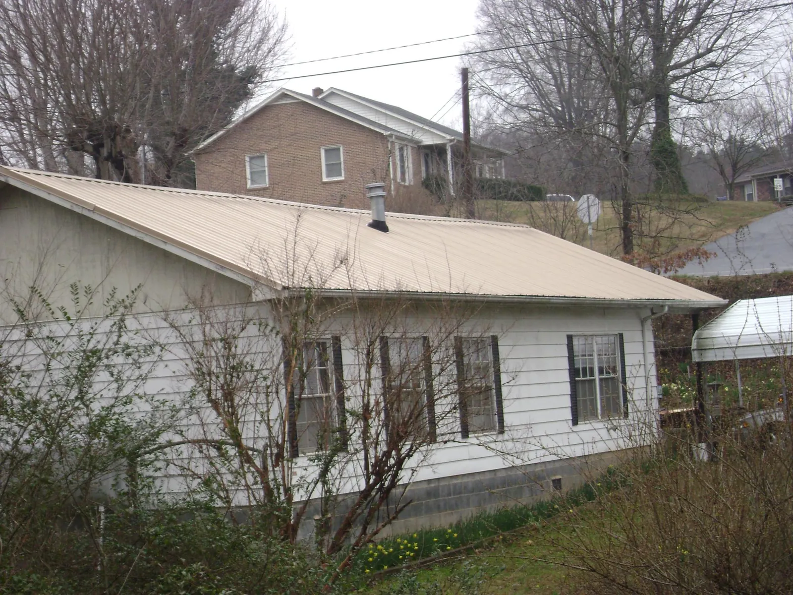 Tan metal roof on a white sided house set into a hillside — Commercial Roofing by Roofing Brothers in Aldrich